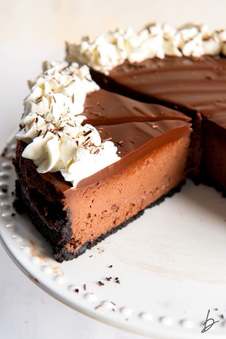 chocolate cheesecake slices garnished with whipped cream on a white cake plate