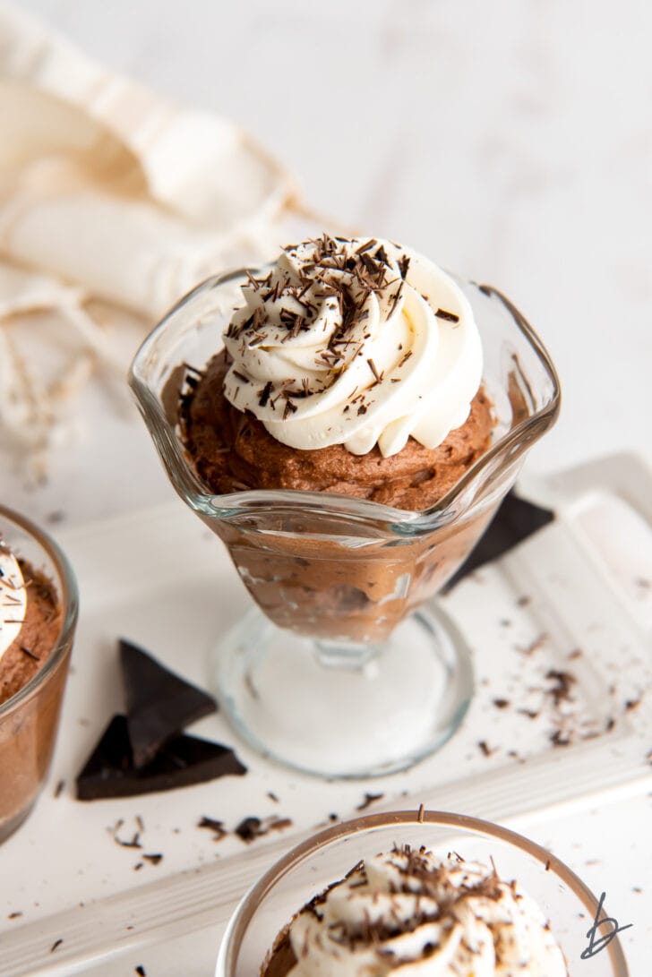 chocolate mousse in a glass ice cream dish with whipped cream and chocolate shavings on top