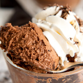 spoon holding bite of chocolate mousse in front of whipped cream on mousse servings