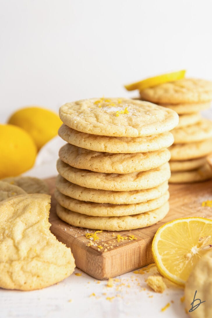 stack of lemon sugar cookies next to lemon wedges and more cookies