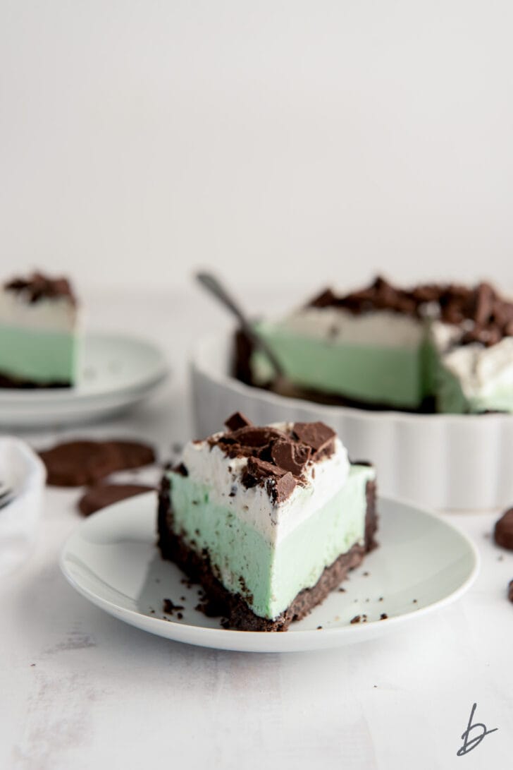 slice of grasshopper pie topped with whipped cream and chocolate cookie bits on a white round plate
