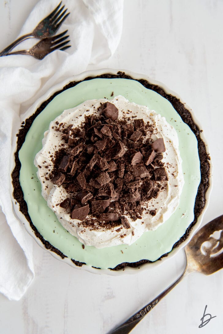 grasshopper pie topped with whipped cream and chopped cookie bits next to white kitchen cloth and pie server