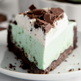 slice of grasshopper pie with layers of chocolate cookie crust, mint cream filling, whipped cream and crushed cookie topping