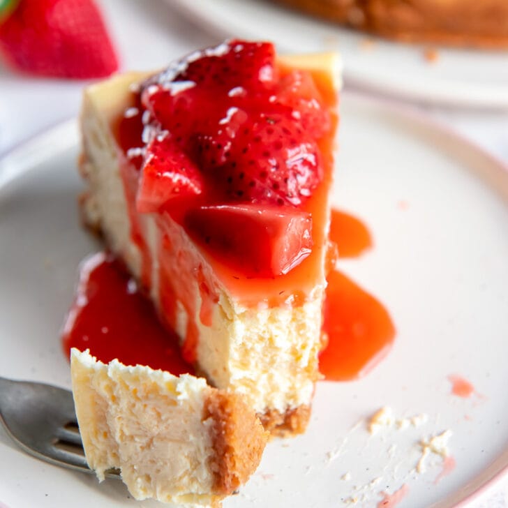 slice of homemade cheesecake topped with strawberry sauce and fork taking bite
