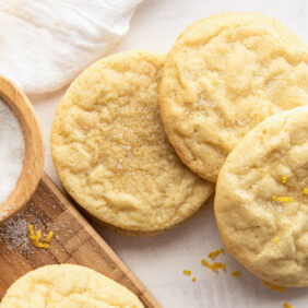 three lemon sugar cookies next to wooden pinch bowl of sugar