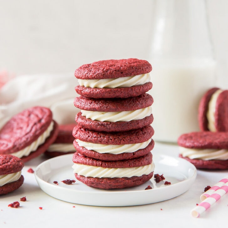 stack of four red velcet sandwich cookies with cream cheese frosting on a small white round plate
