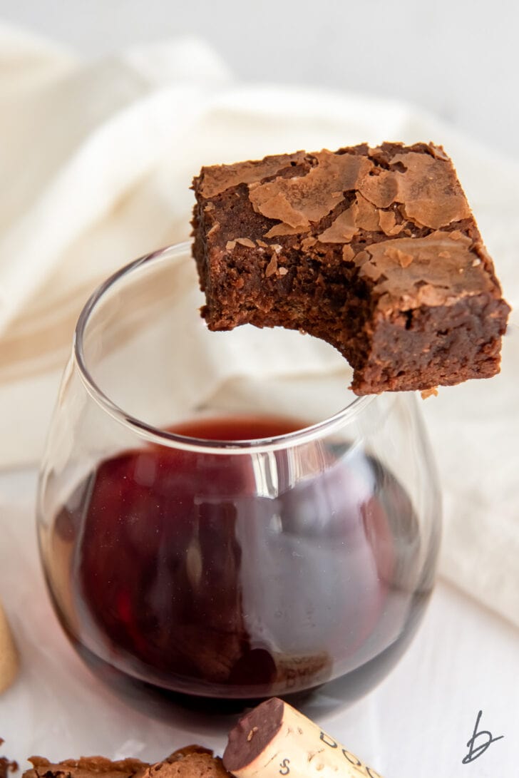 red wine brownie with a bite sitting on edge of stemless glass with red wine