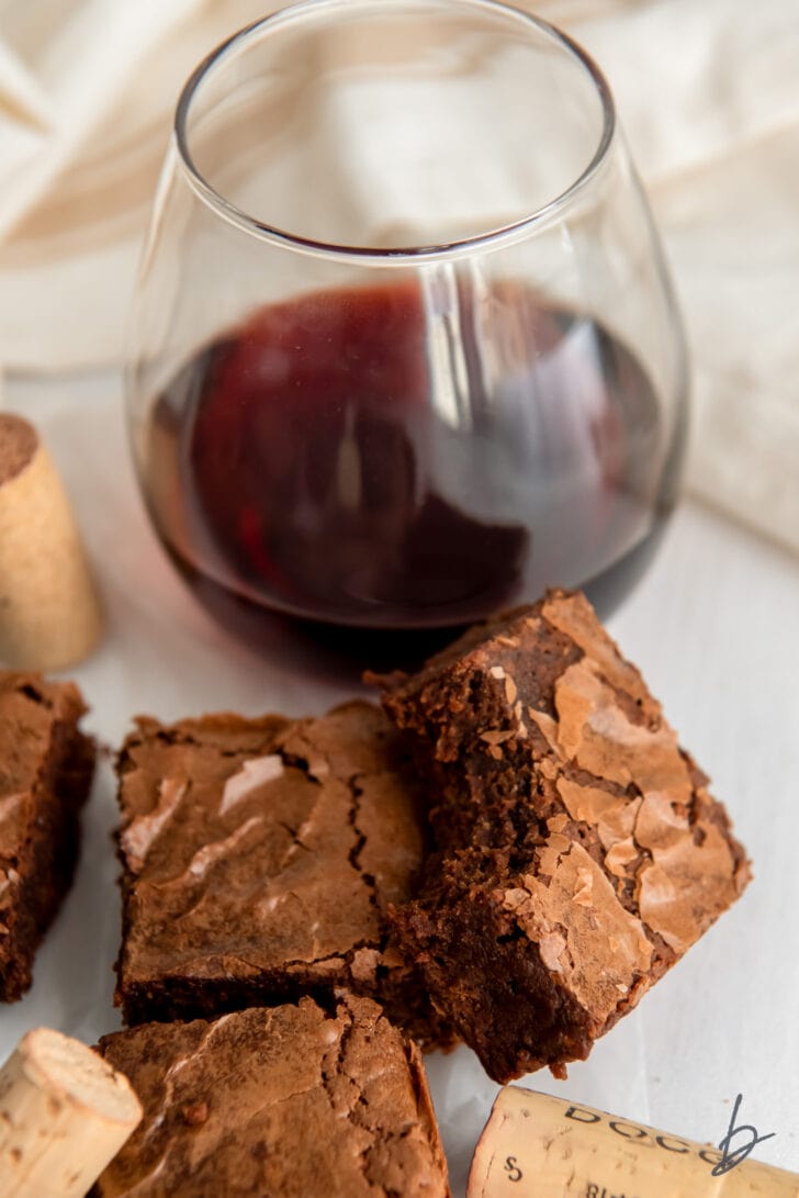 red wine brownie with a bite leaning on another brownie in front of stemless glass of red wine