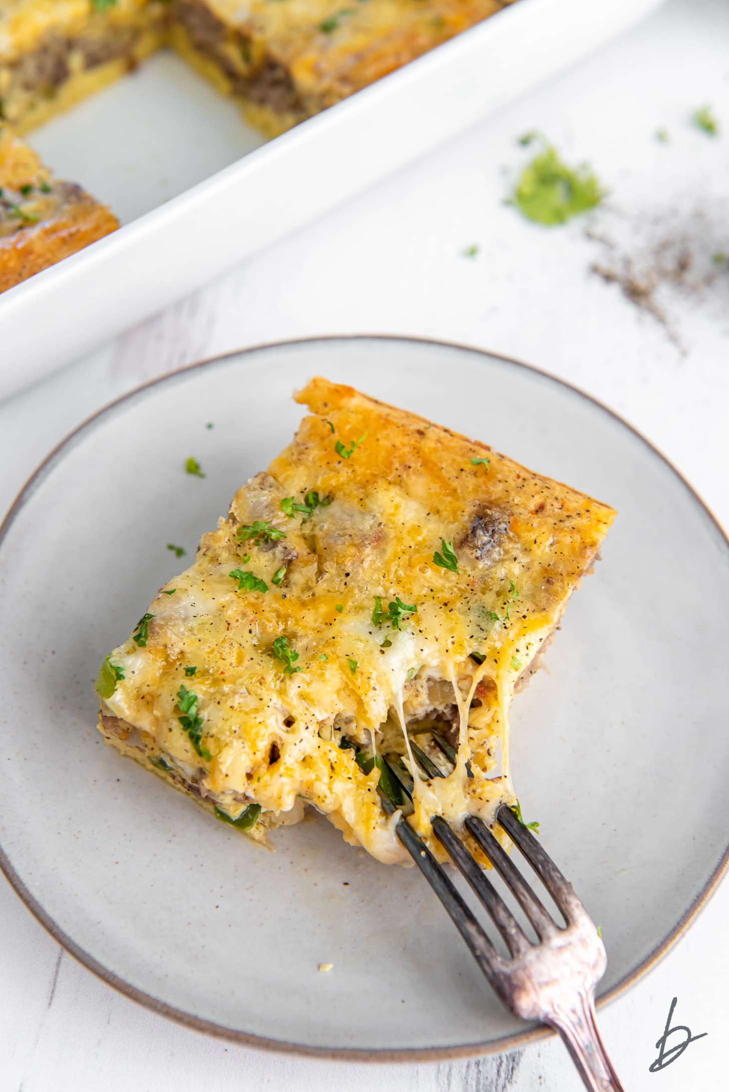 fork pulling a bite off slice of sausage breakfast casserole on a plate