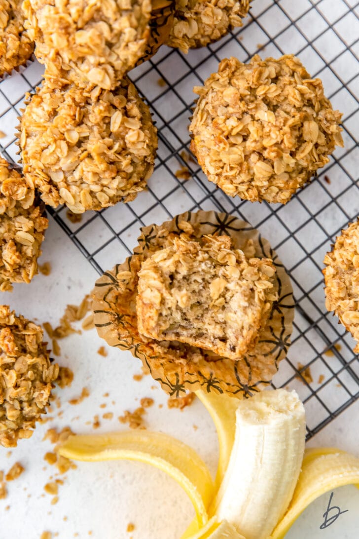 banana oatmeal muffin with a bite on open paper liner next to more muffins and a banana with a bite