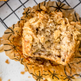 banana oatmeal muffin with a bite on open paper muffin liner on wire cooling rack