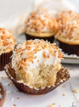 coconut cupcakes garnished with toasted coconut with a bite taken out of cupcake