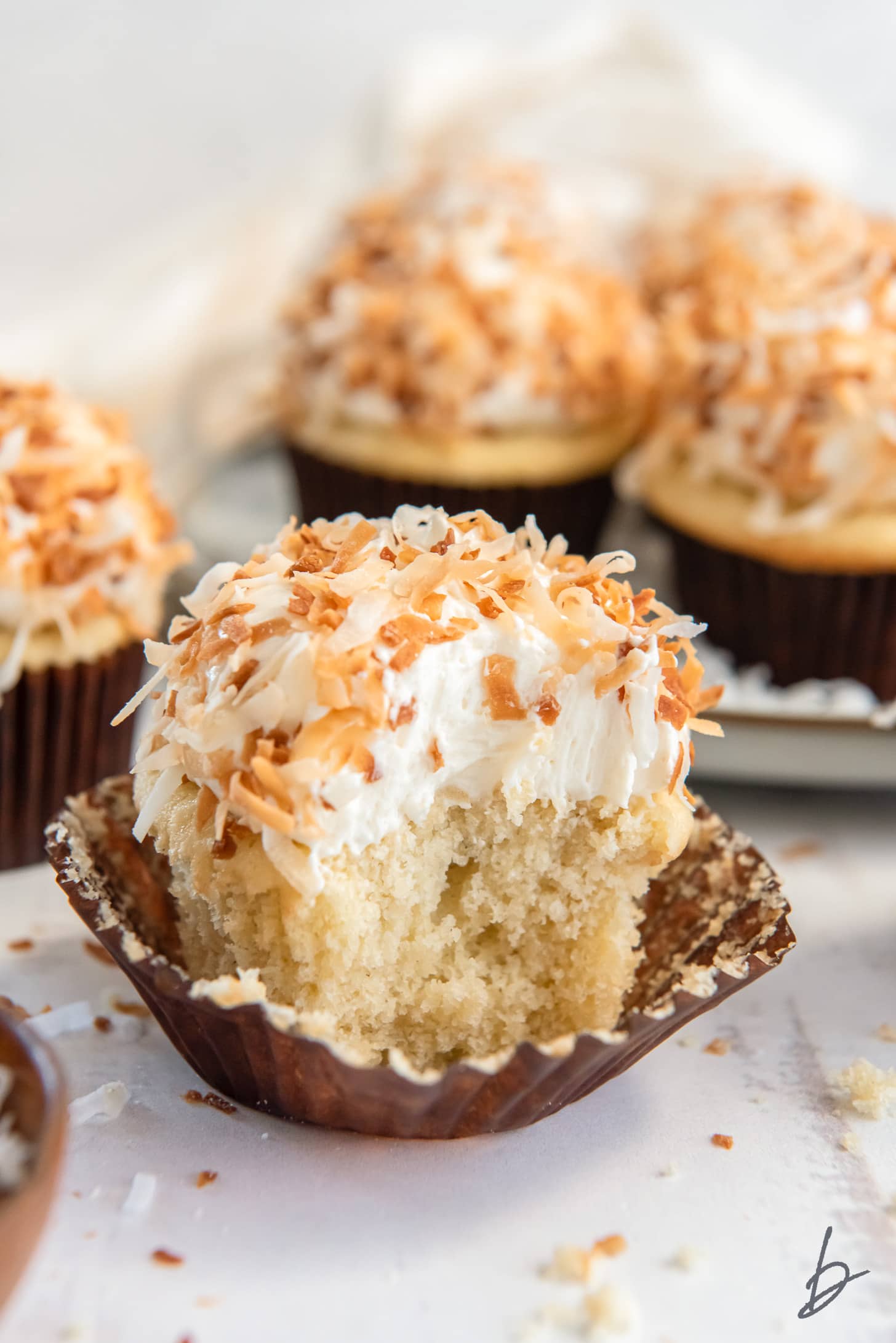 coconut cupcakes garnished with toasted coconut with a bite taken out of cupcake