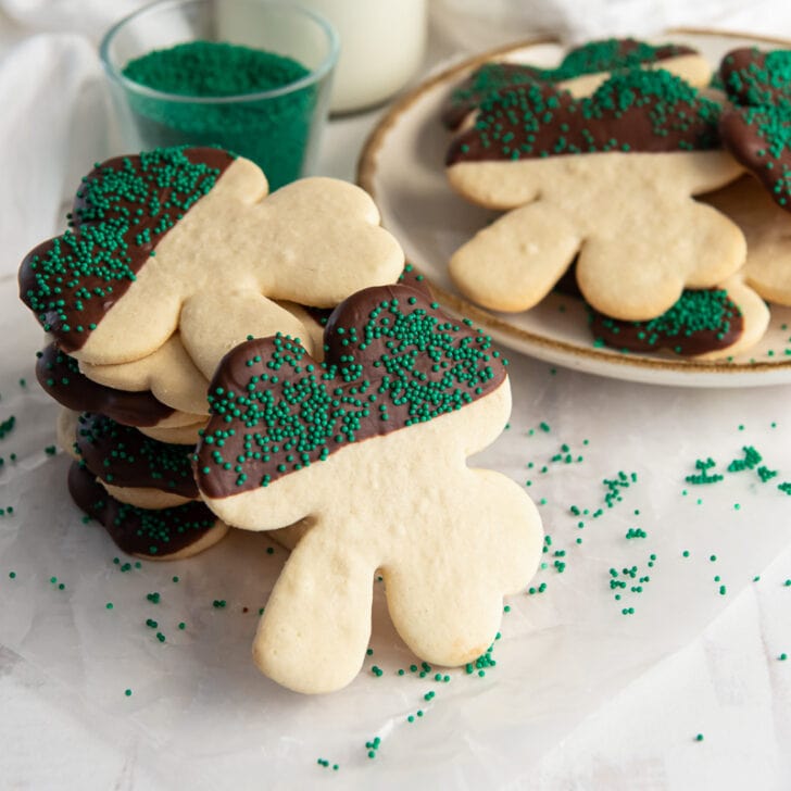 shamrock sugar cookie half covered in chocolate and green sprinkles leaning on more cookies