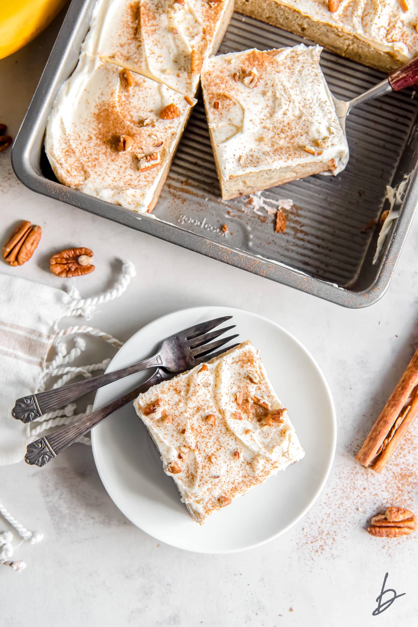 square slice of banana cake on white plate with fork next to a rectangle pan with more cake