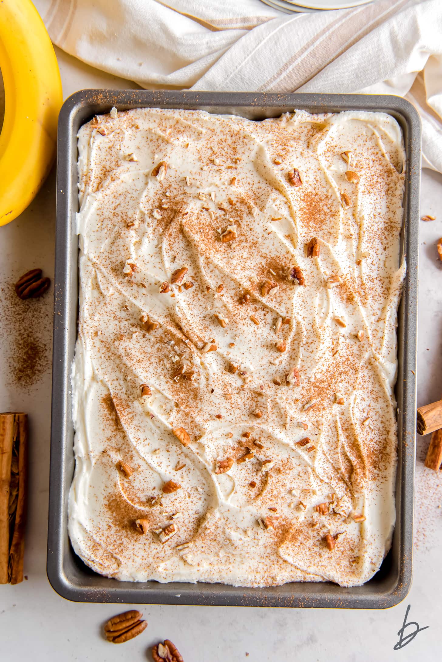 banana cake with cream cheese frosting and dusting of cinnamon in a 9-inch by 13-inch cake pan