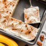 banana cake with cream cheese frosting in a sheet cake pan with one slice cut away from cake