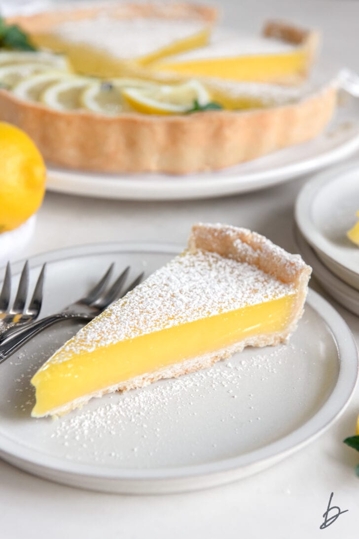 lemon curd tart slice on a white round plate with dessert forks