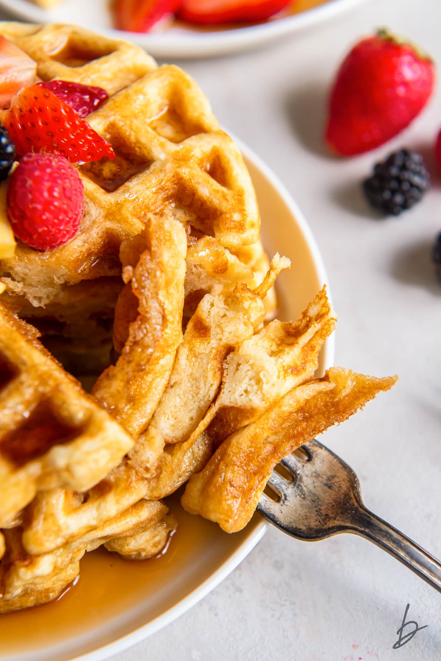 fork holding bite of buttermilk waffles on plate