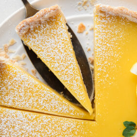lemon curd tart with two slices cut and pie server under one slice