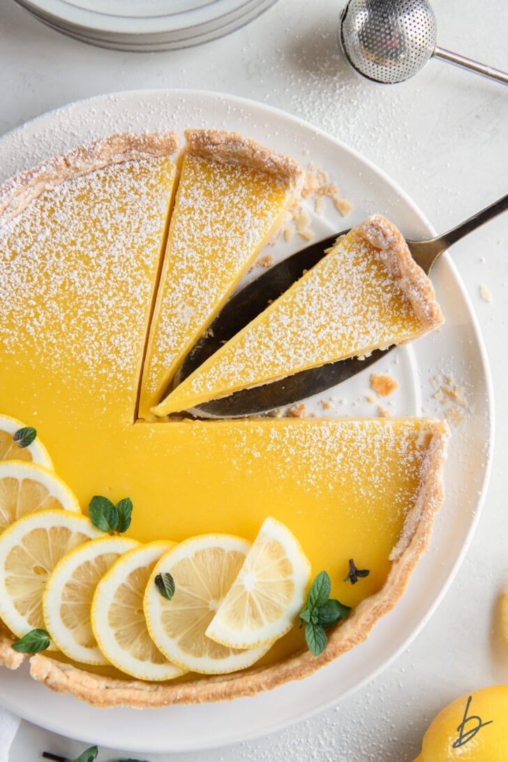 lemon curd tart garnished with lemon slices and two slices cut from tart