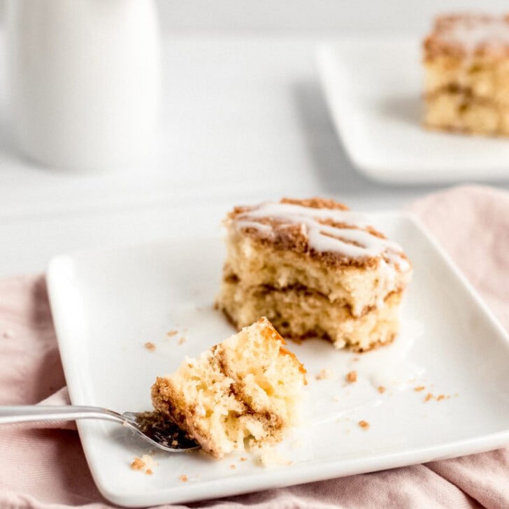 piece of sour cream coffee cake with fork holding bite on white square plate