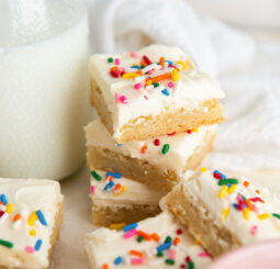 stack of frosted sugar cookie bars with rainbow sprinkles next to a glass milk bottle