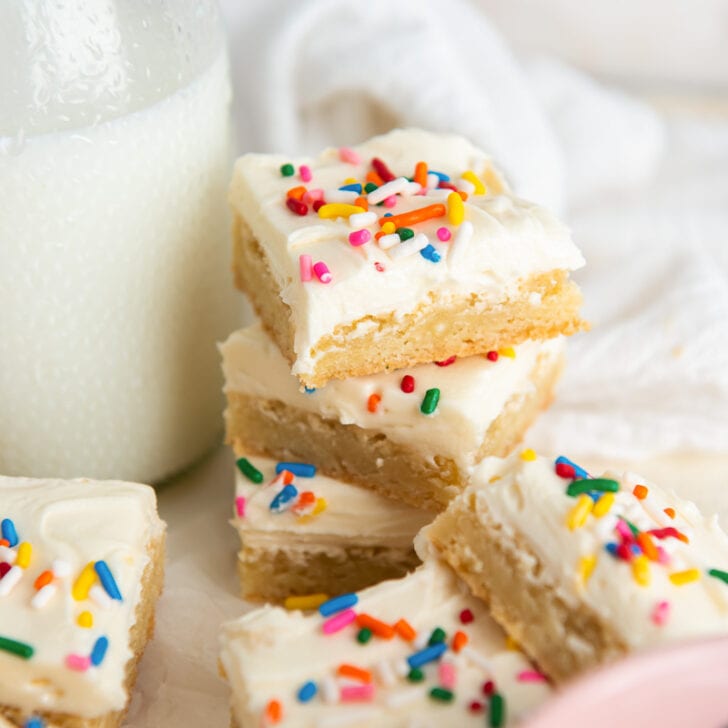 stack of frosted sugar cookie bars with rainbow sprinkles next to a glass milk bottle