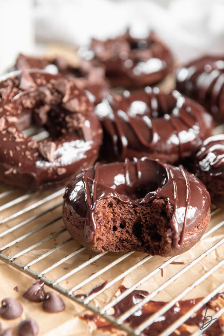 baked chocolate donut with a bite in front of more chocolate glazed donuts