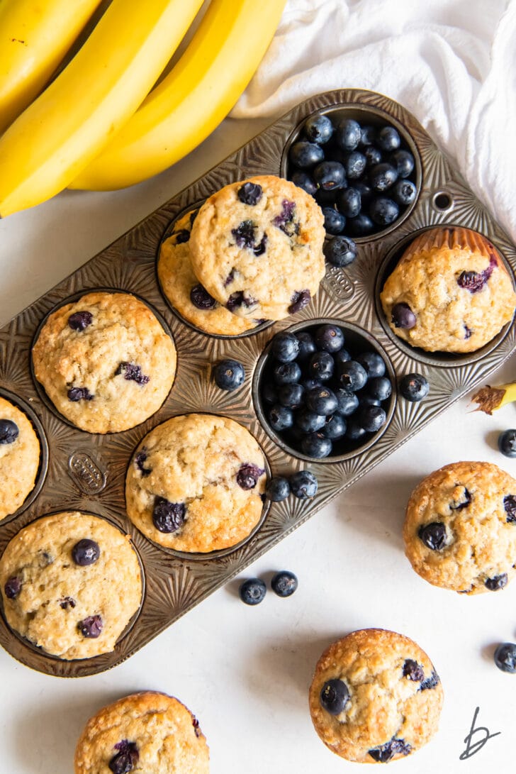 blueberry banana muffins in a muffin tin and one muffin cup filled with fresh blueberries