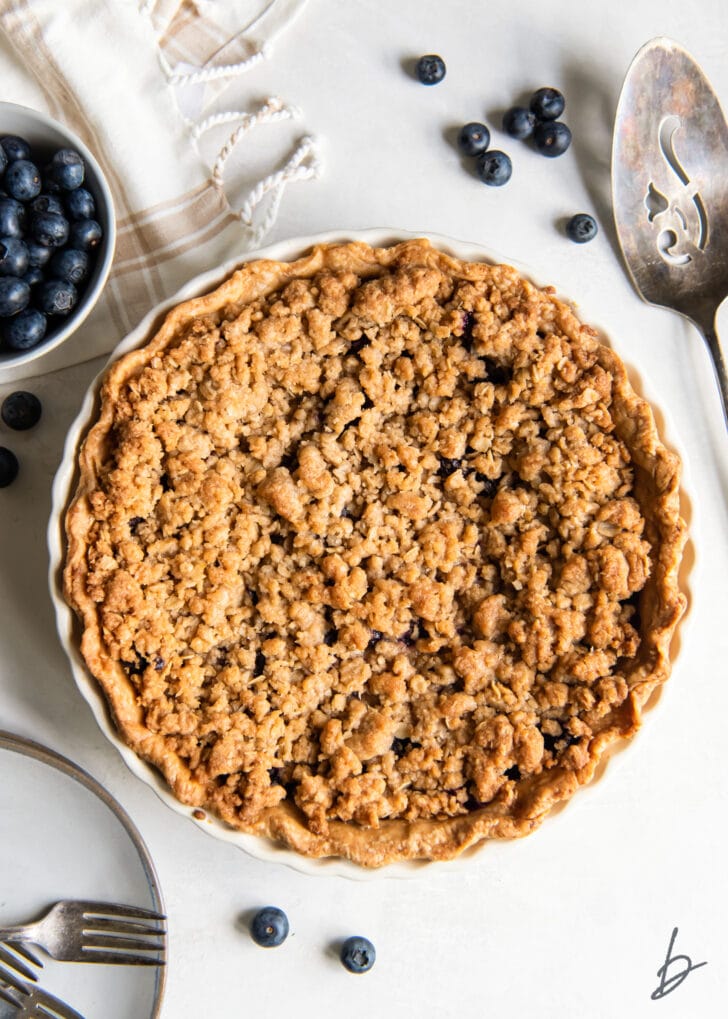 uncut blueberry crumble pie next to blueberries and pie server