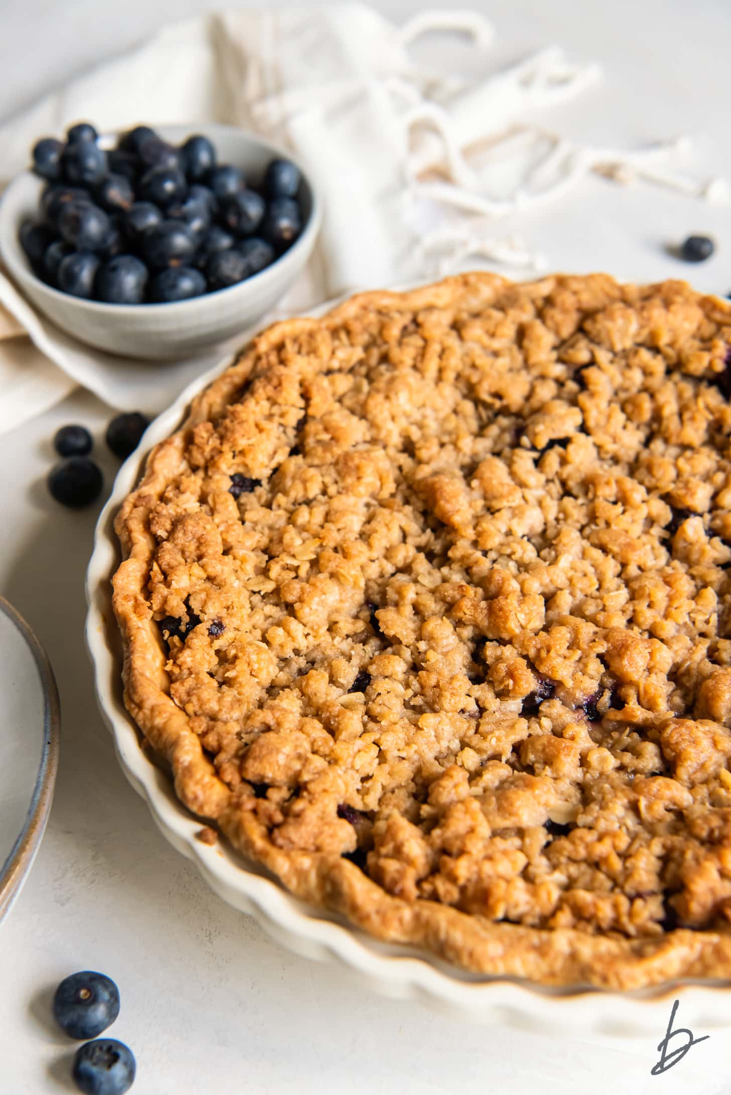 blueberry crumble pie next to bowl of fresh blueberries