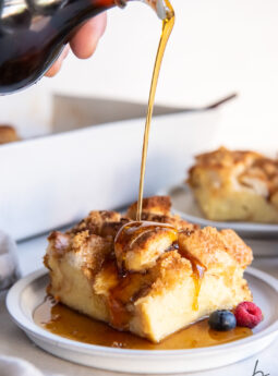maple syrup being poured over square slice of french toast casserole on round white plate