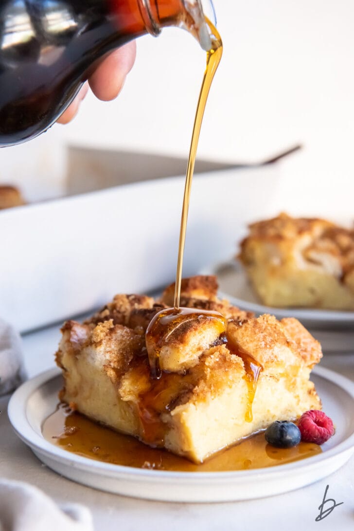 maple syrup being poured over square slice of french toast casserole on round white plate