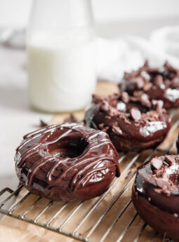 baked chocolate donut with chocolate glaze on corner of wire cooling rack in front of glass milk jug