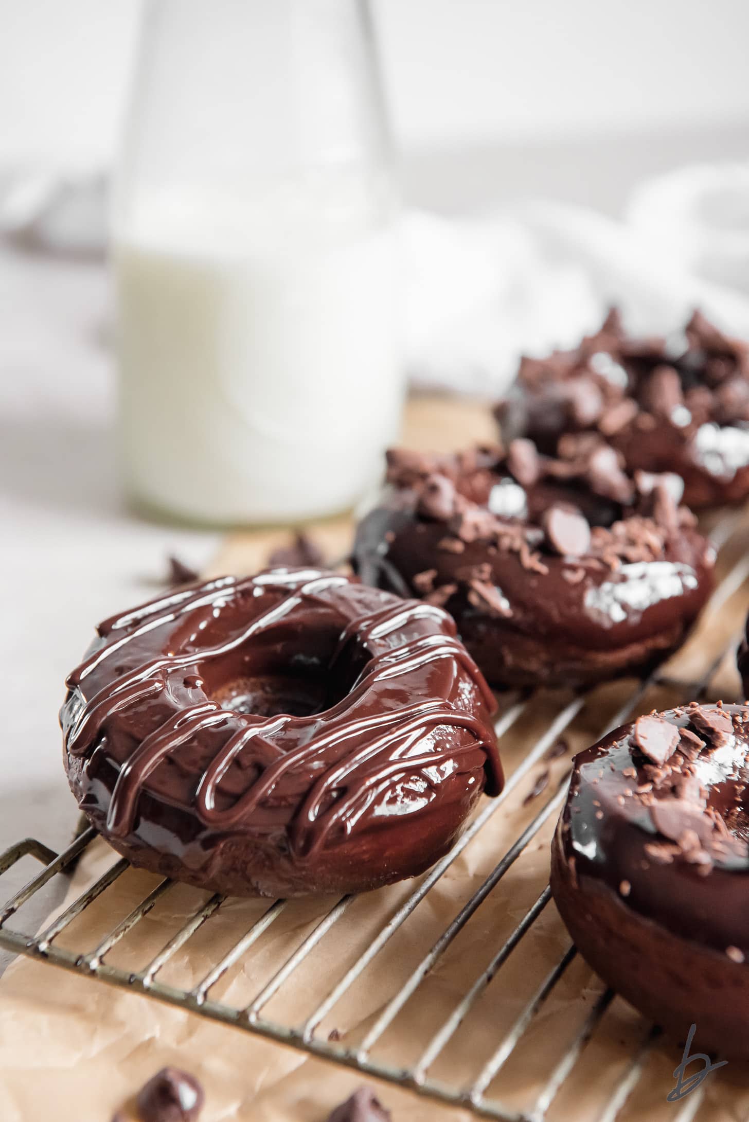baked chocolate donut with chocolate glaze on corner of wire cooling rack in front of glass milk jug