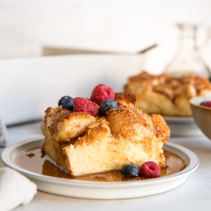 square slice of french toast casserole on a plate with maple syrup and fresh berries