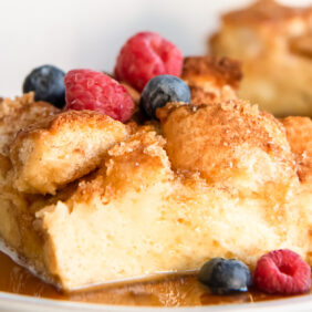 square slice of french toast casserole topped with berries and sitting on plate with maple syrup