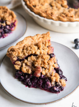 slice of blueberry crumble pie will juicy filling on round grey plate