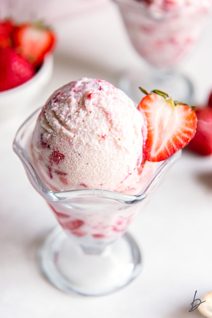 homemade strawberry ice cream in a glass dish with a fresh strawberry half