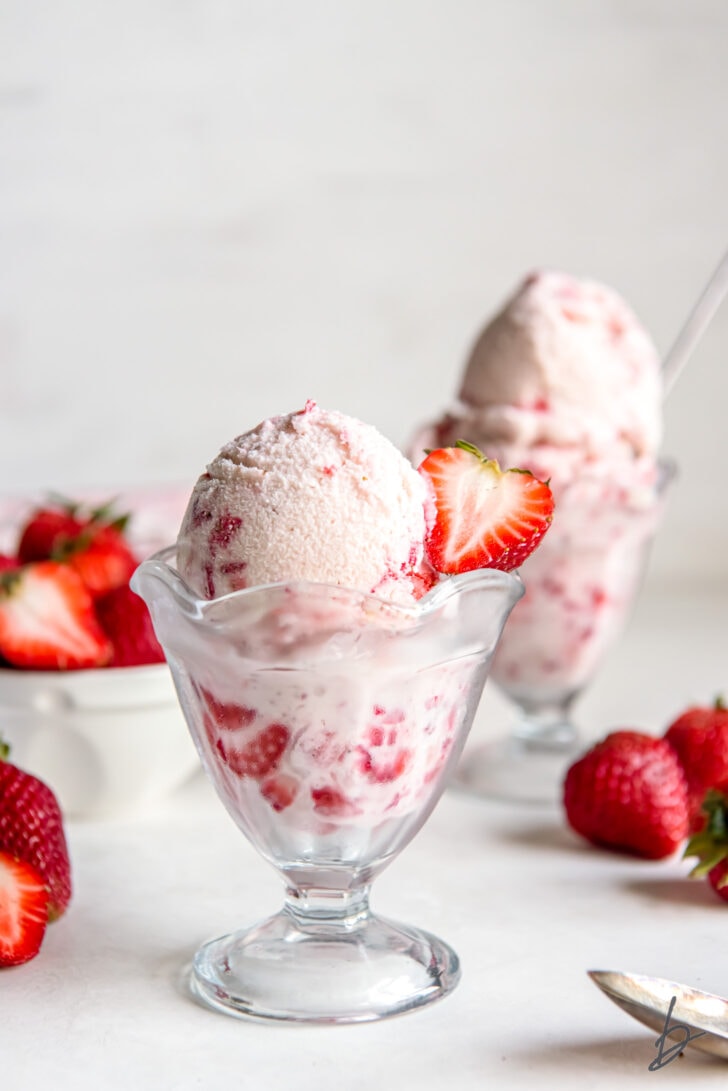 strawberry ice cream in a glass sundae dish with a fresh strawberry garnish