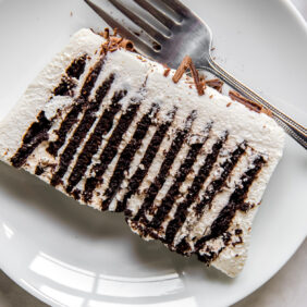 slice of icebox cake with chocolate wafers and whipped cream on a white round plate