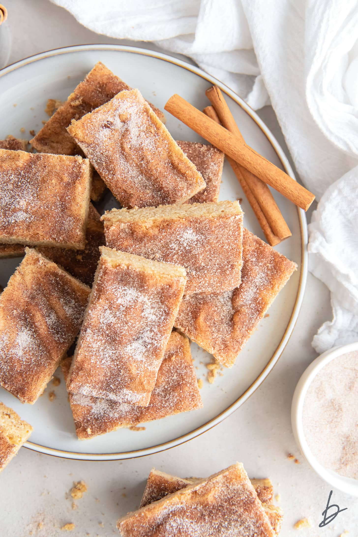 cinnamon sugar coated snickerdoodle bars on a round plate with cinnamon sticks