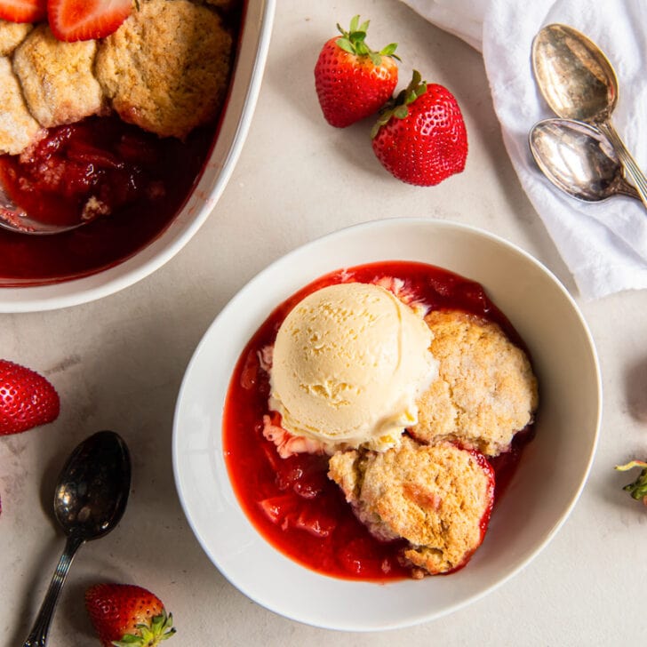 strawberry cobbler in a bowl with a scoop of vanilla ice cream and lots of strawberry juices