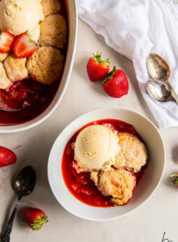 bowl of strawberry cobbler topped with a scoop of vanilla ice cream in a bowl