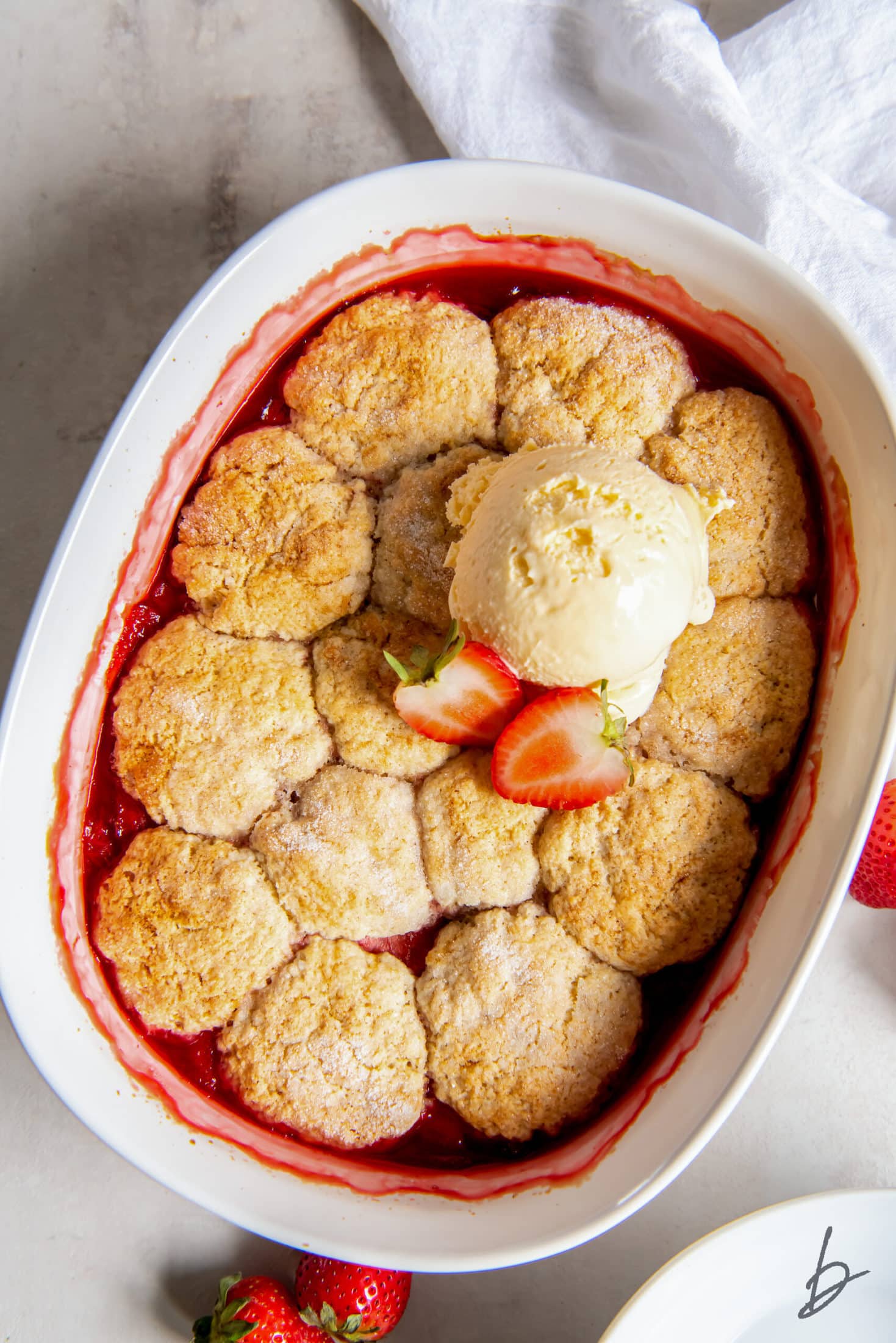 one scoop of vanilla ice cream on top of strawberry cobbler in a white baking dish