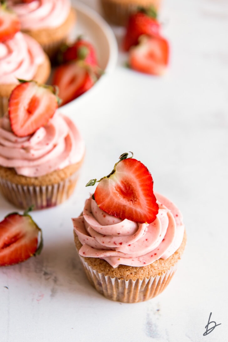 strawberry cupcake topped with pink cream cheese frosting and a strawberry half
