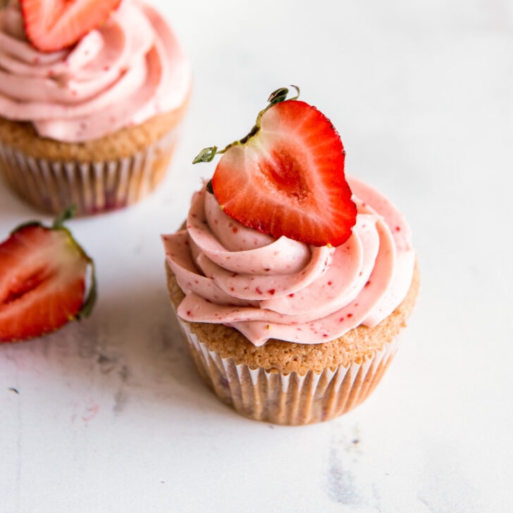 strawberry cupcake topped with pink strawberry cream cheese frosting and fresh strawberry half