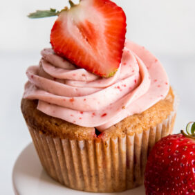 strawberry cupcake with pink frosting and half a strawberry garnish