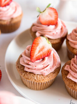 strawberry cupcakes with pink frosting and fresh strawberry garnish on a plate